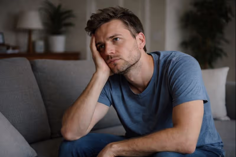 Adult sitting indoors with a tense posture and unfocused expression
